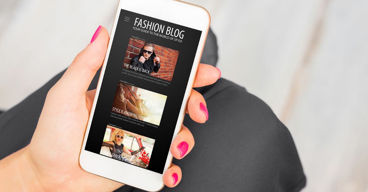 A woman holds a mobile phone in her hand as she surfs a fashion blog from its screen.