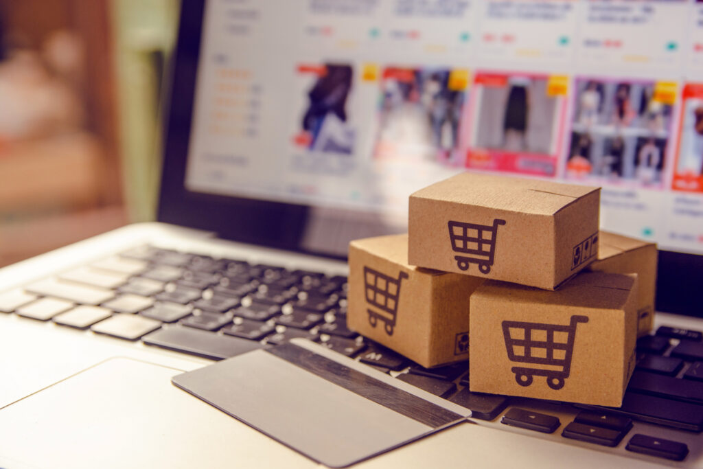 A laptop sits open with an e-commerce website for clothing on the screen. Small cardboard boxes with shopping carts drawn on them represent the power of Albuquerque SEO techniques for ecommerce brands. 