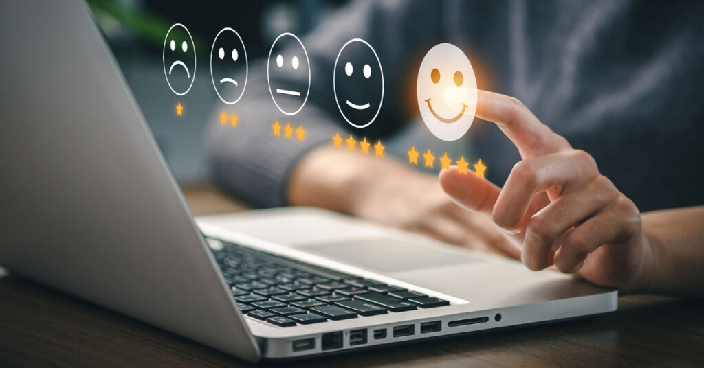 A man sits at a laptop computer viewing a website. We see emojis projected in front of him with different expressions. He is choosing the one with a smiling face. 